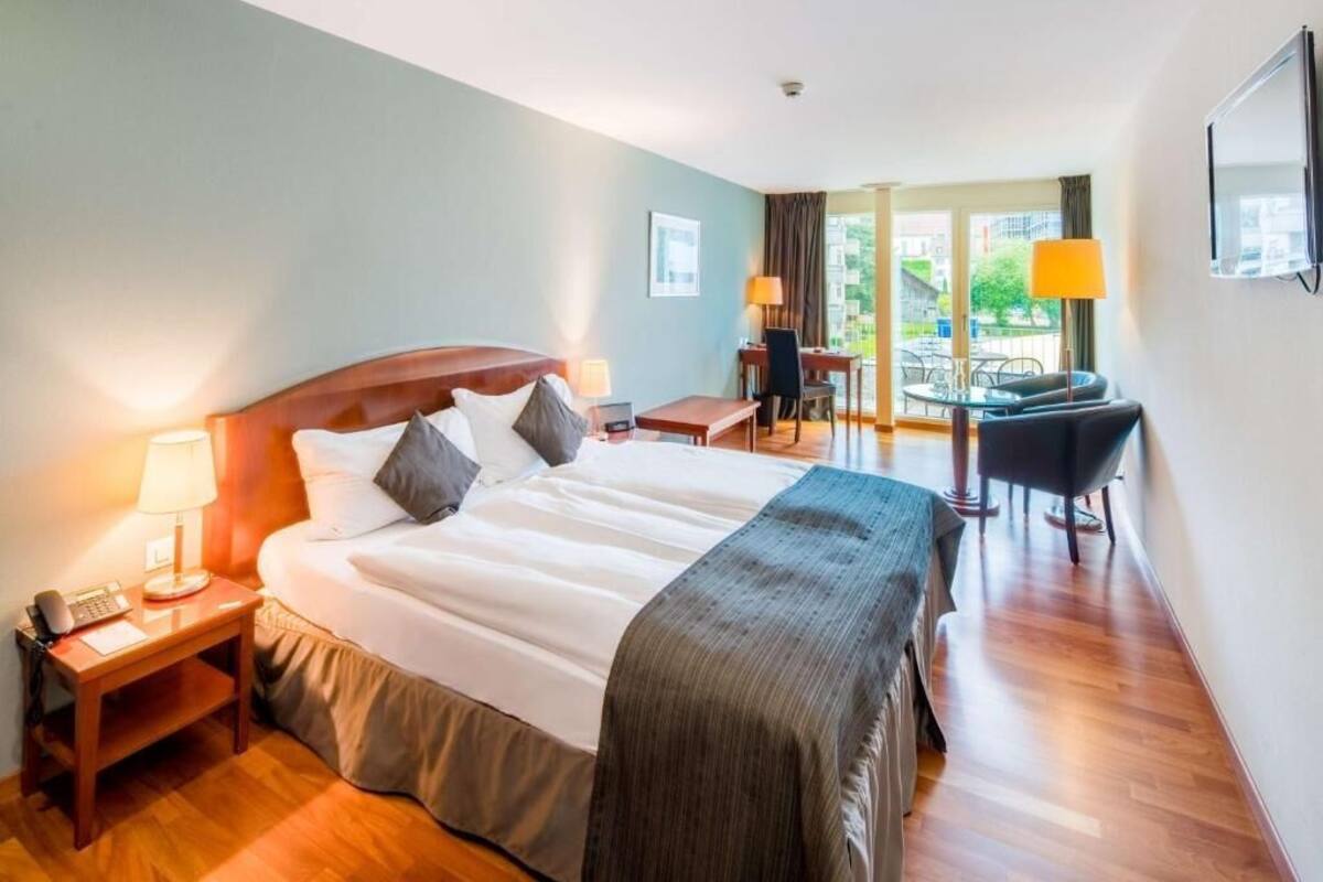 A hotel room with a large bed, a desk, a chair, and a balcony with a view.
