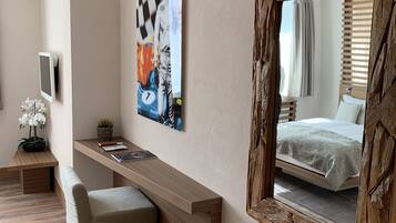 A modern bedroom with a large mirror, a bedside table, a bench, and a wall-mounted TV.
