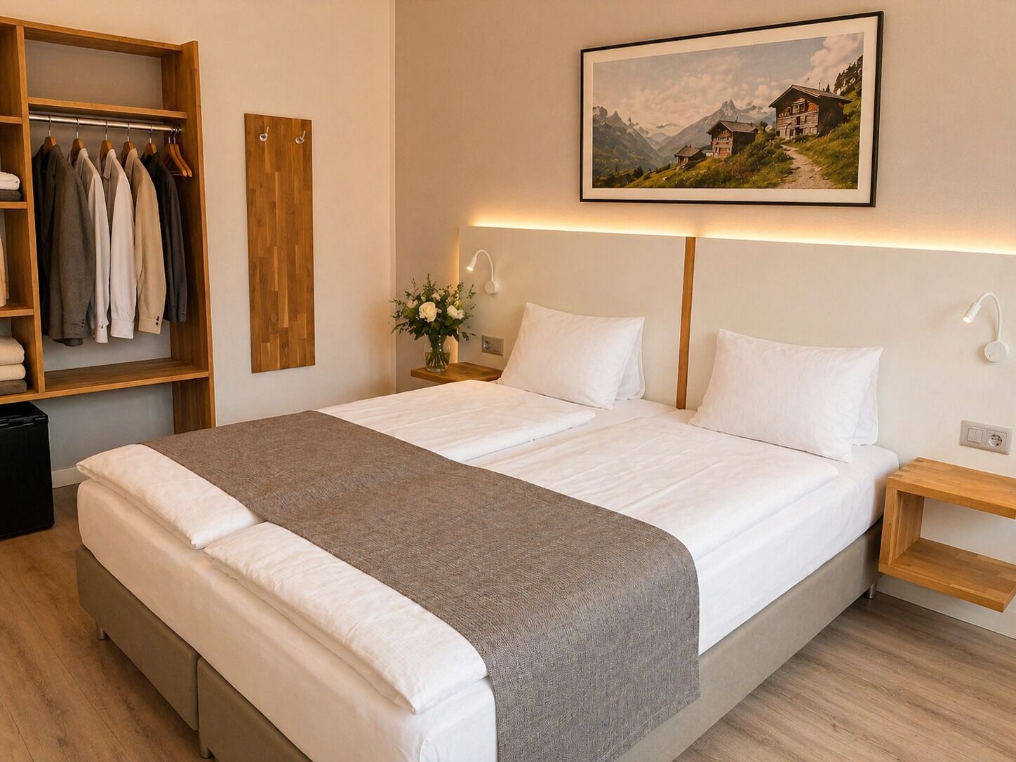 A neatly arranged hotel room with a large bed, a wooden wardrobe, a bedside table with a lamp, and a framed picture on the wall.