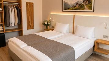 A neatly arranged hotel room with a large bed, a wooden wardrobe, a bedside table with a lamp, and a framed picture on the wall.