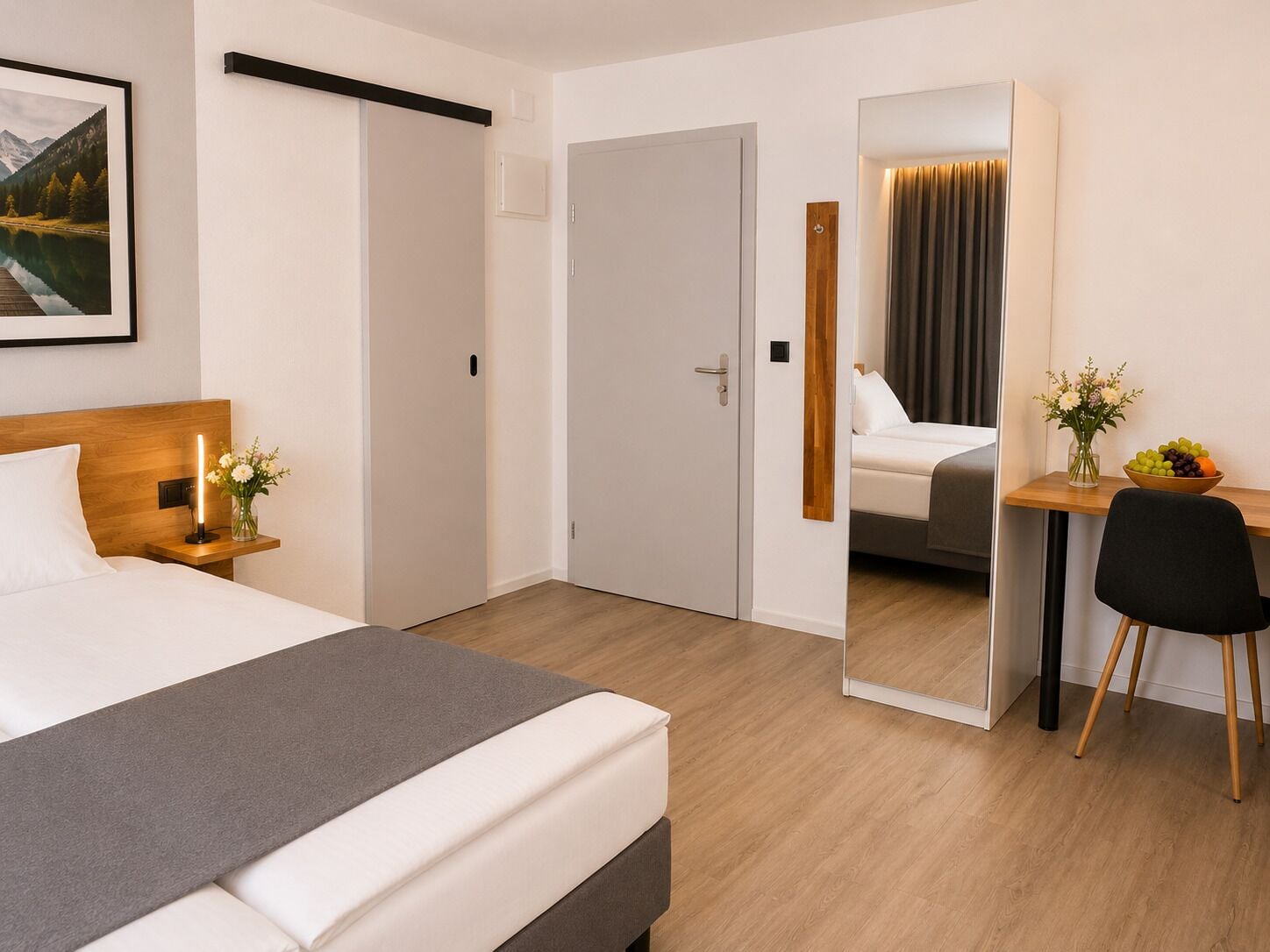 A hotel room with a bed, bedside table, mirror, desk, chair, and a view of the bathroom.