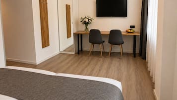 A hotel room with a bed, a desk with two chairs, a TV, and a small table with fruit.