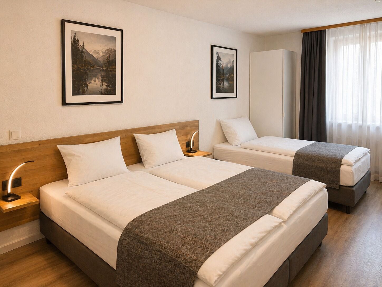 A hotel room with two beds, a wooden headboard, a nightstand, a lamp, a wardrobe, and two framed pictures on the wall.