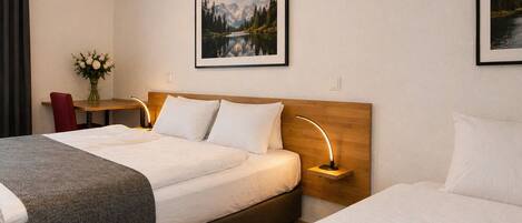 Habitación de hotel con dos camas, un escritorio, una silla, un jarrón de flores y dos cuadros en la pared.