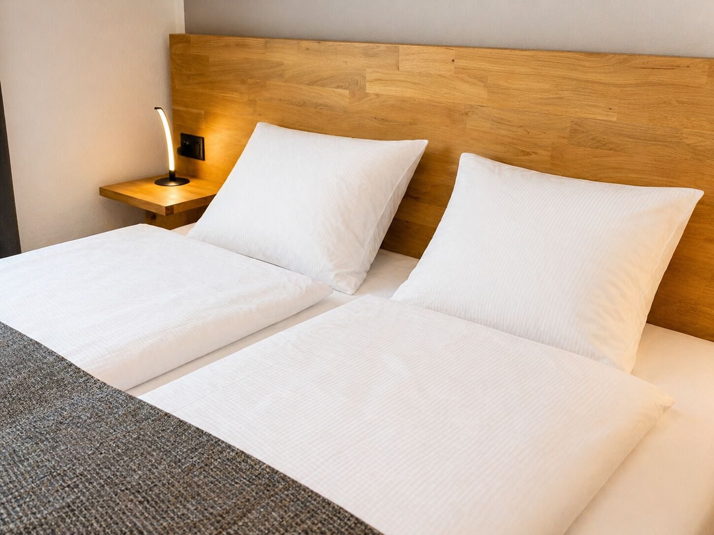 Una cama doble con sábanas blancas, un cabecero de madera y una mesita de noche con lámpara.