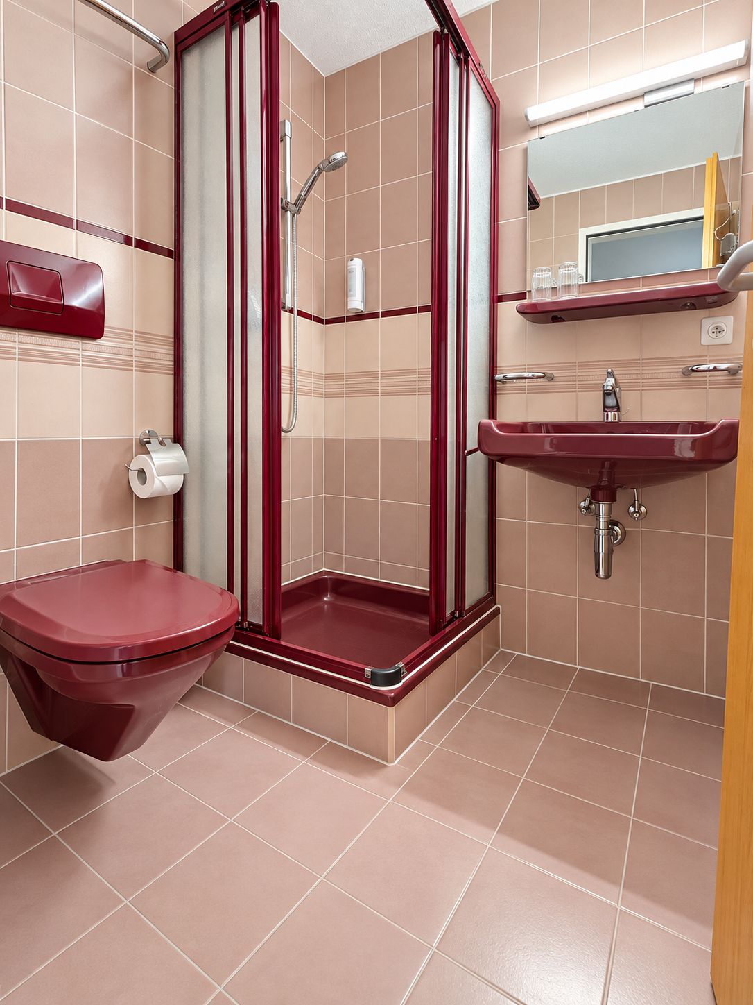 Un baño con inodoro rojo, cabina de ducha y lavamanos.