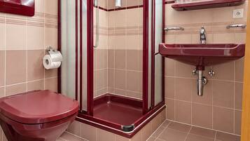 Un baño con inodoro rojo, cabina de ducha y lavamanos.