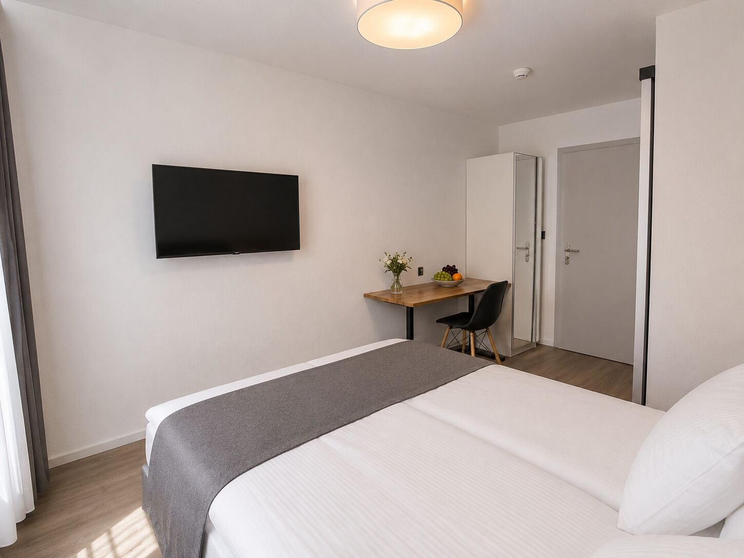 A hotel room with a bed, a desk with a chair, a television, and a door.