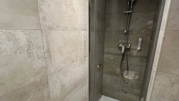 Una ducha moderna con mampara de vidrio, una toalla blanca y un cabezal de ducha de mano.
