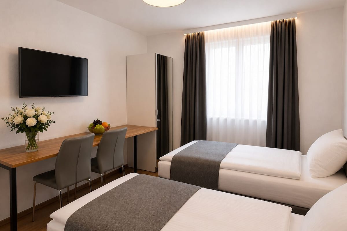 Ein Hotelzimmer mit zwei Betten, einem Schreibtisch mit Stuhl, einem Fernseher und einem Fenster mit Vorhängen.