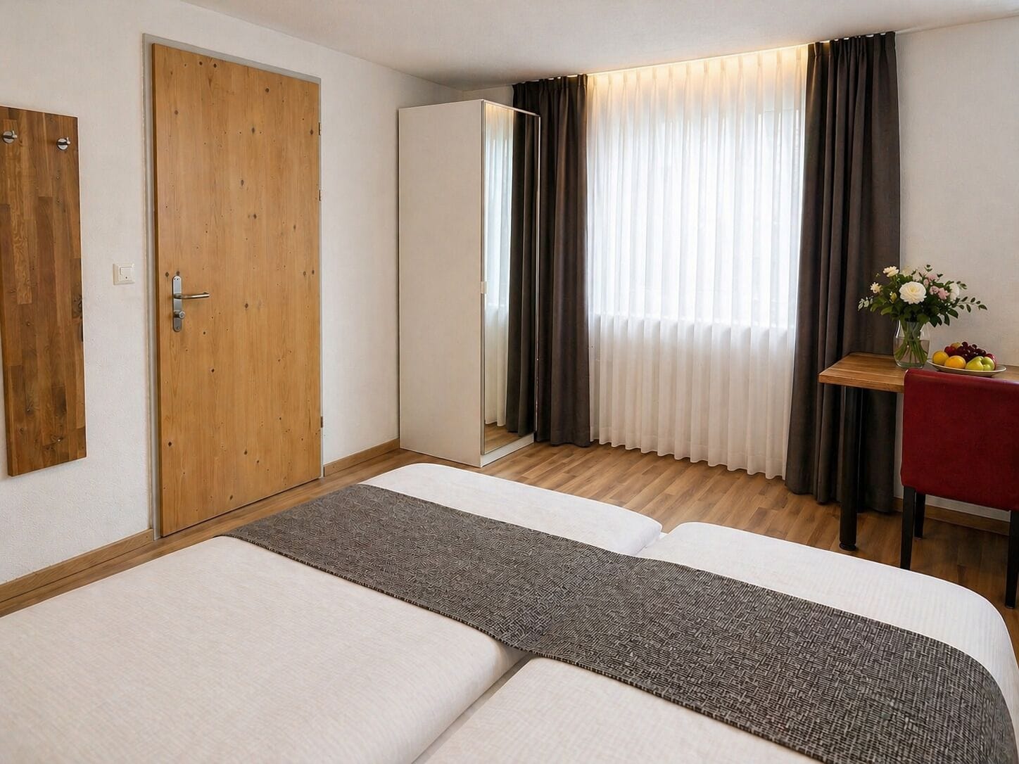 Una habitación de hotel con una cama, una puerta de madera y un escritorio con un florero.