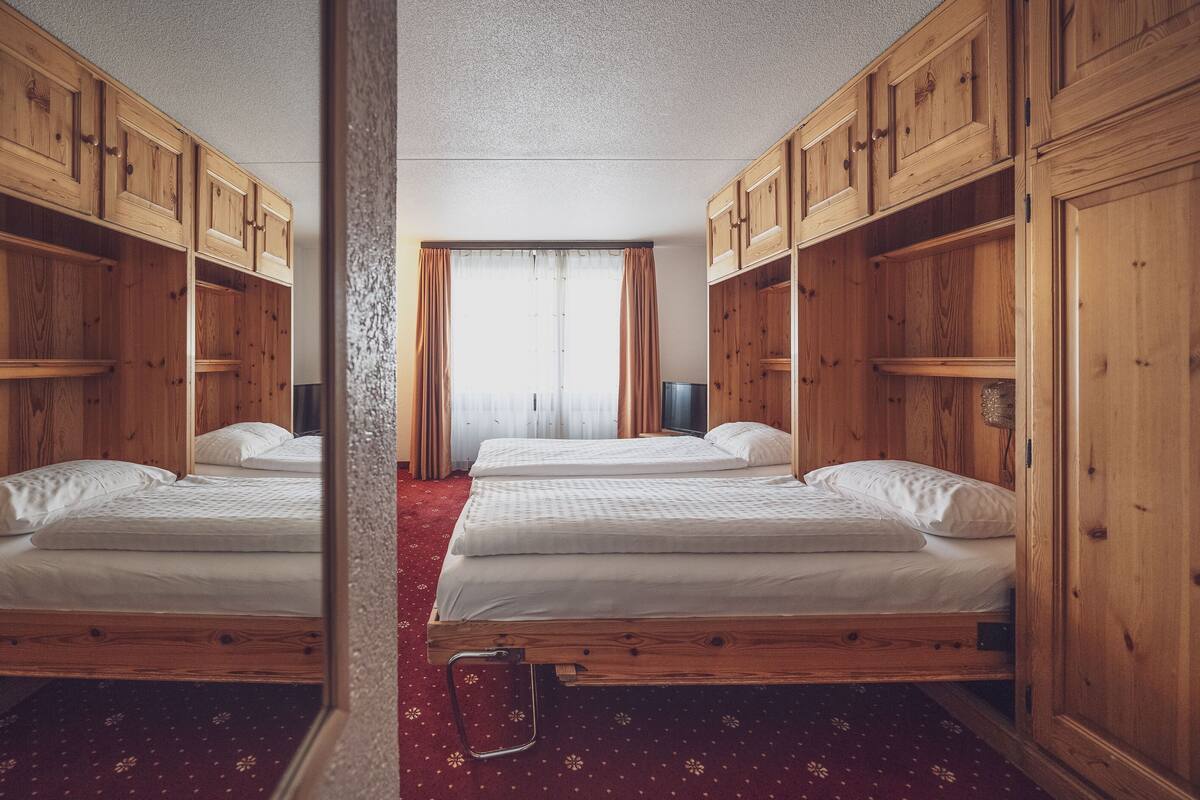 A room with two beds, wooden cabinets, and a red carpet.