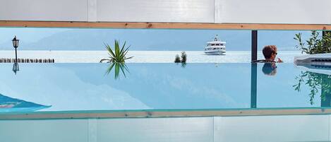 A room with a large window overlooking a body of water, a boat, and distant mountains.
