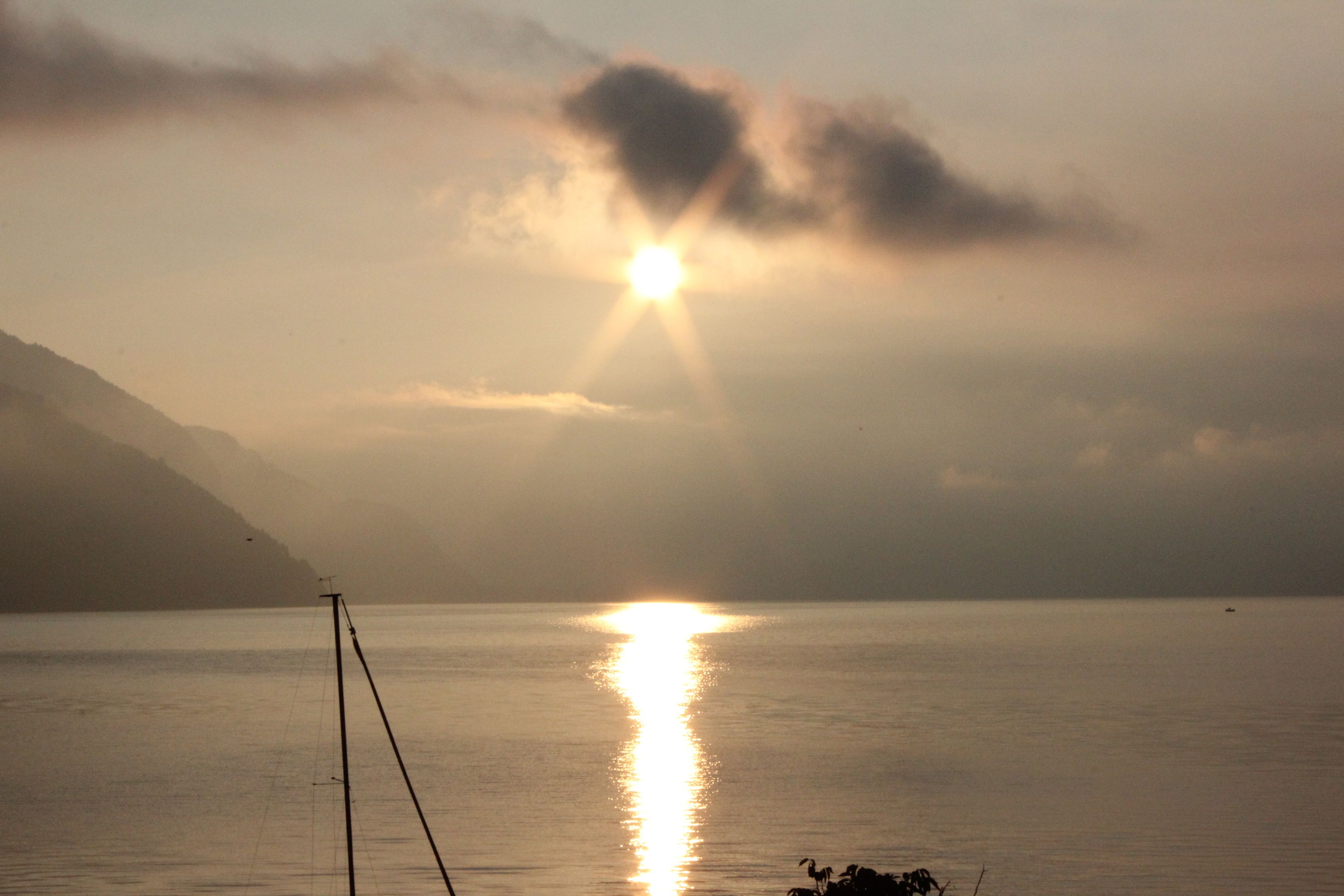 Une étendue d’eau calme, où le soleil se reflète à la surface, une montagne lointaine et un petit bateau.
