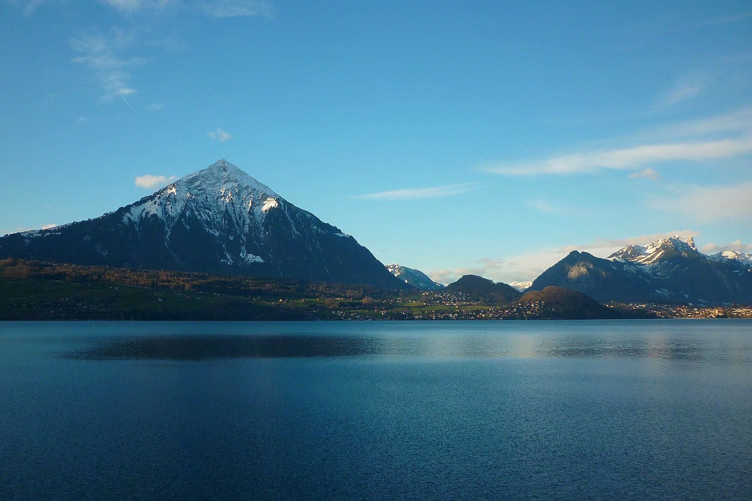 A mountain landscape with a lake in the foreground and a small town in the midground.