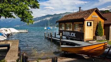 A wooden cabin with a sign reading "SEEBLICK" by a calm lake with boats docked.