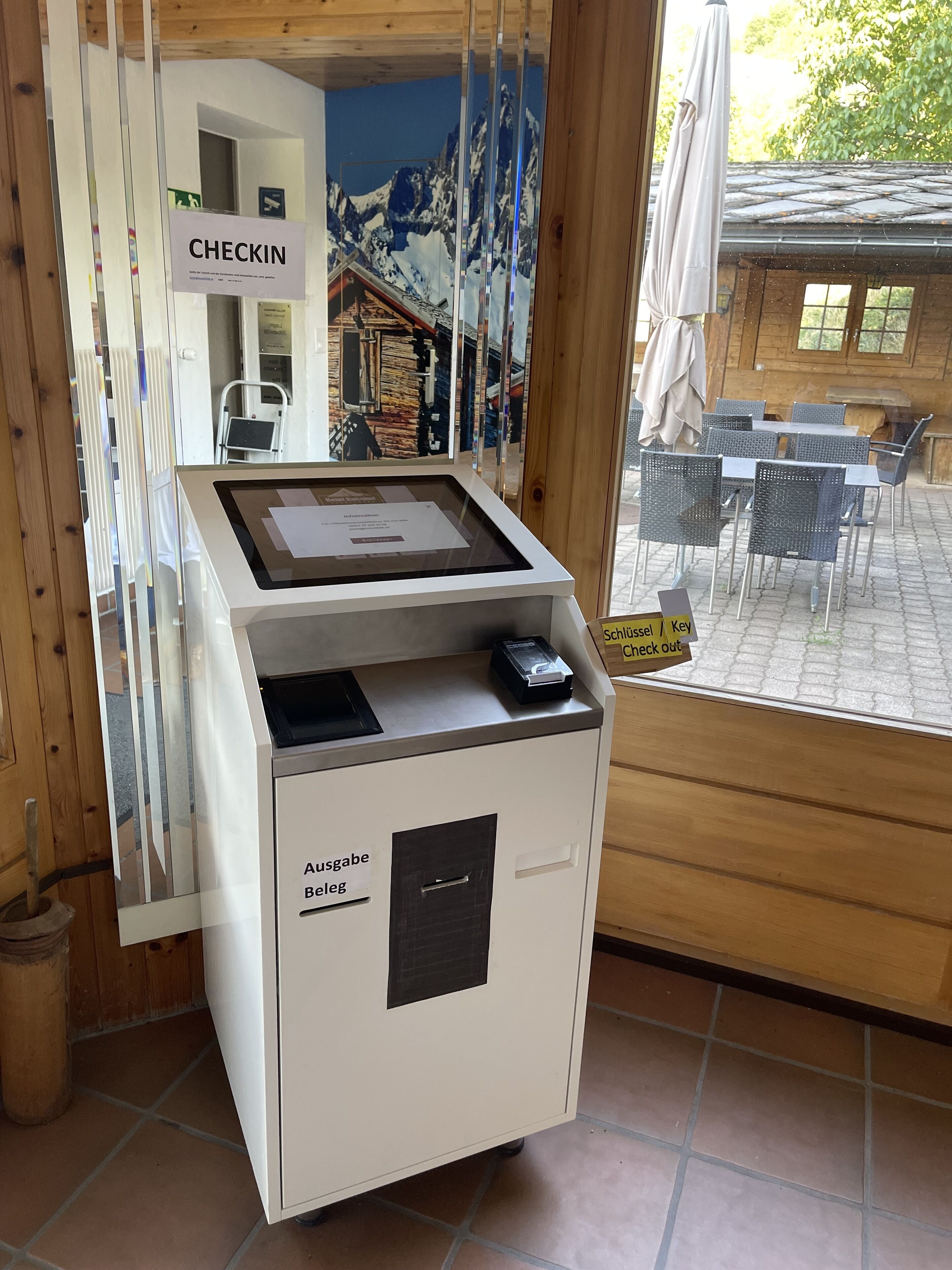 A reception desk with a 'CHECKIN' sign, a digital display, and a 'Schlüssel / Key' sign indicating a key check-out area.