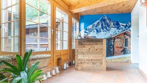 Interior de madera con ventanas amplias, un mural de montañas y una planta.