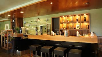 A bar area with a wooden counter, bar stools, shelves with bottles and glasses, and a clock on the wall.