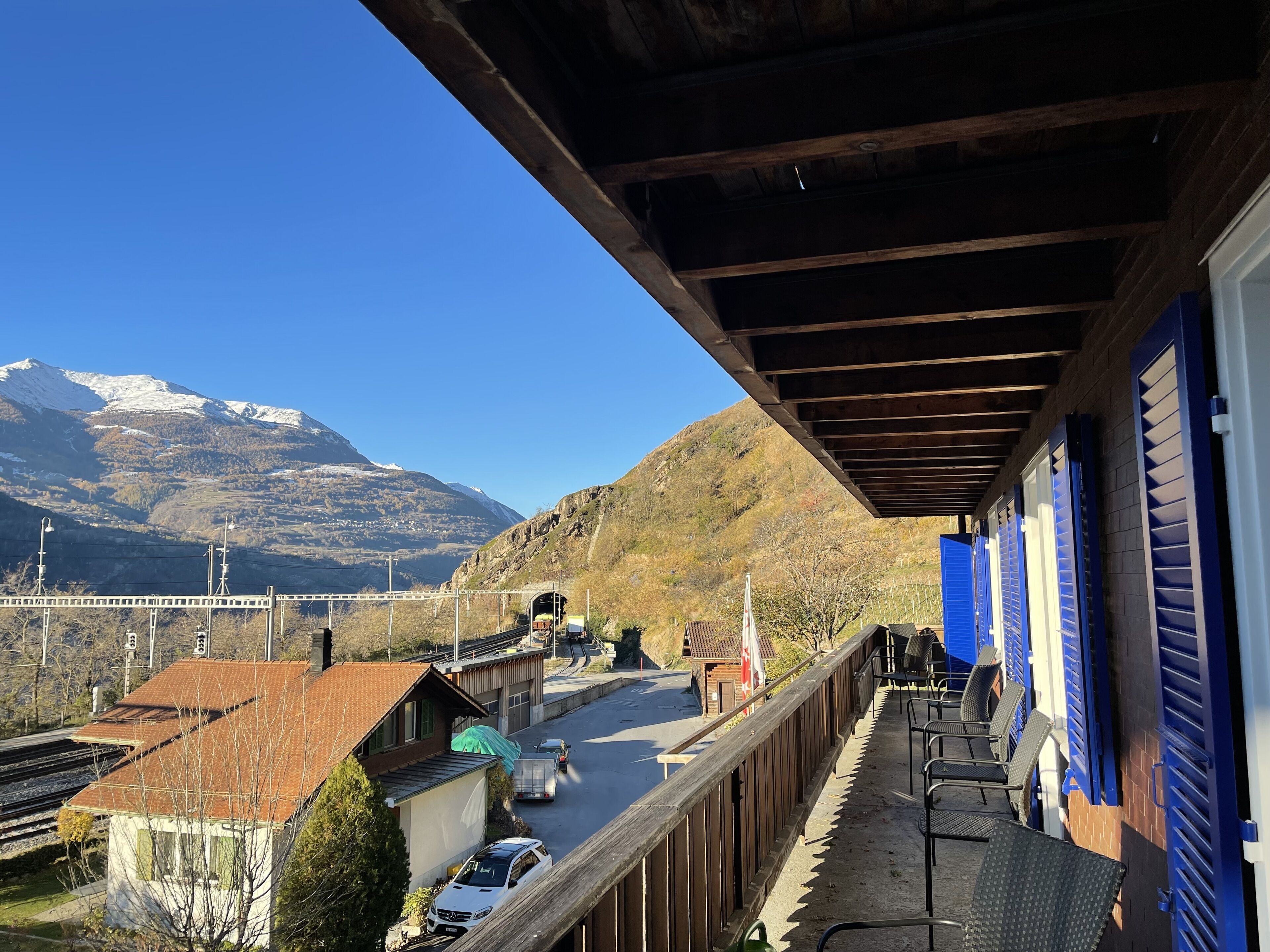A balcony with a mountain view, a train track, and a building with blue shutters.