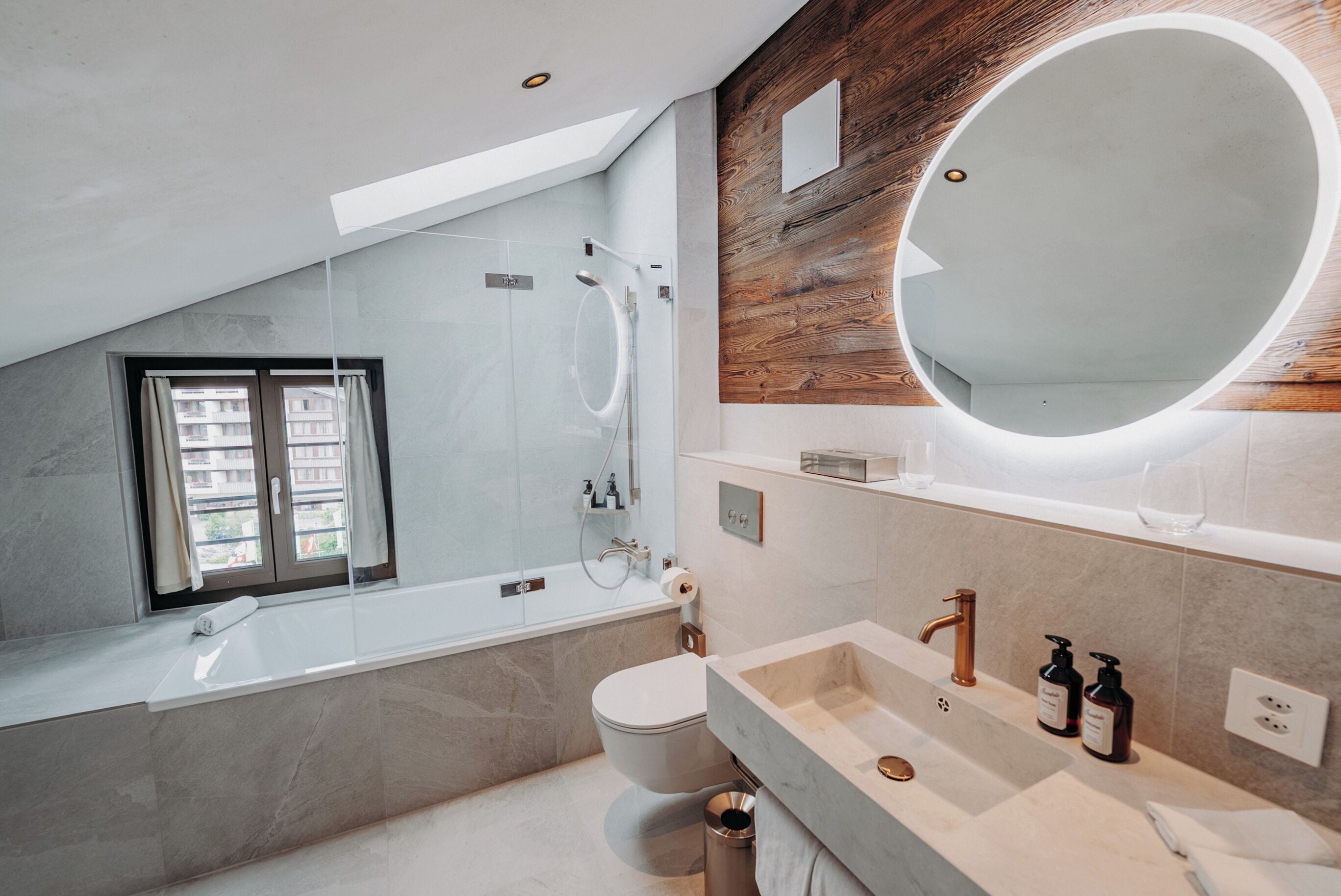 Un baño moderno con tragaluz, una bañera independiente, un espejo grande y un tocador con lavamanos y dos dispensadores de jabón.