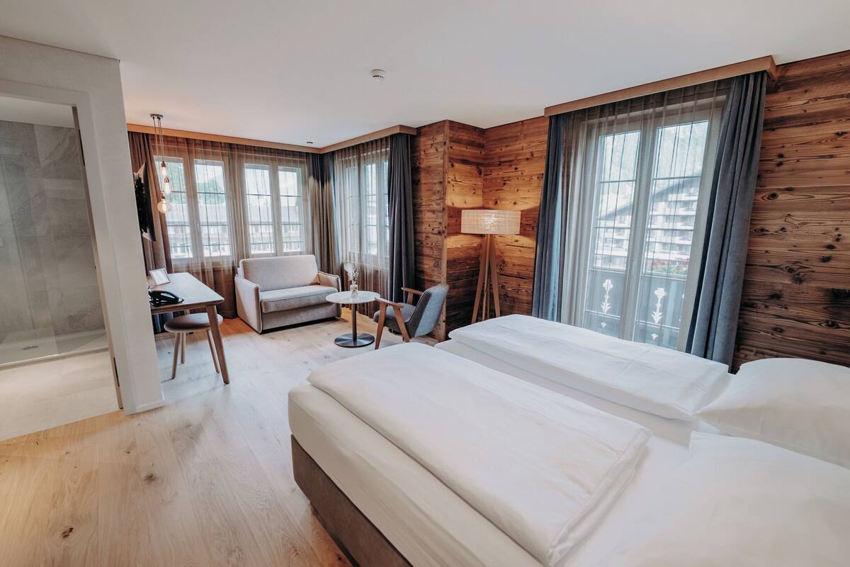 A hotel room with a large bed, a desk, a chair, and a small table.
