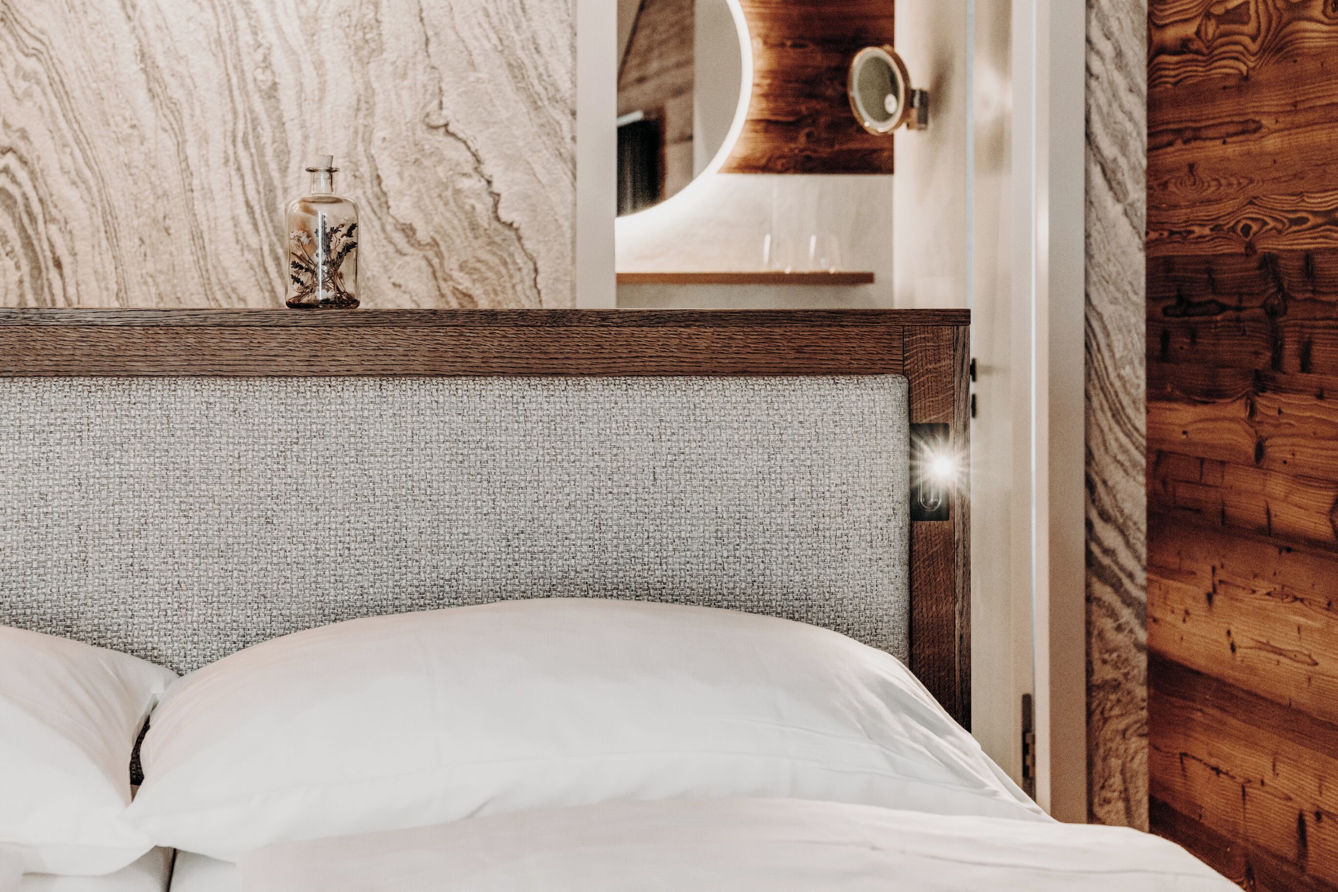 Una cama con sábanas blancas, cabecera de madera y pared con textura.