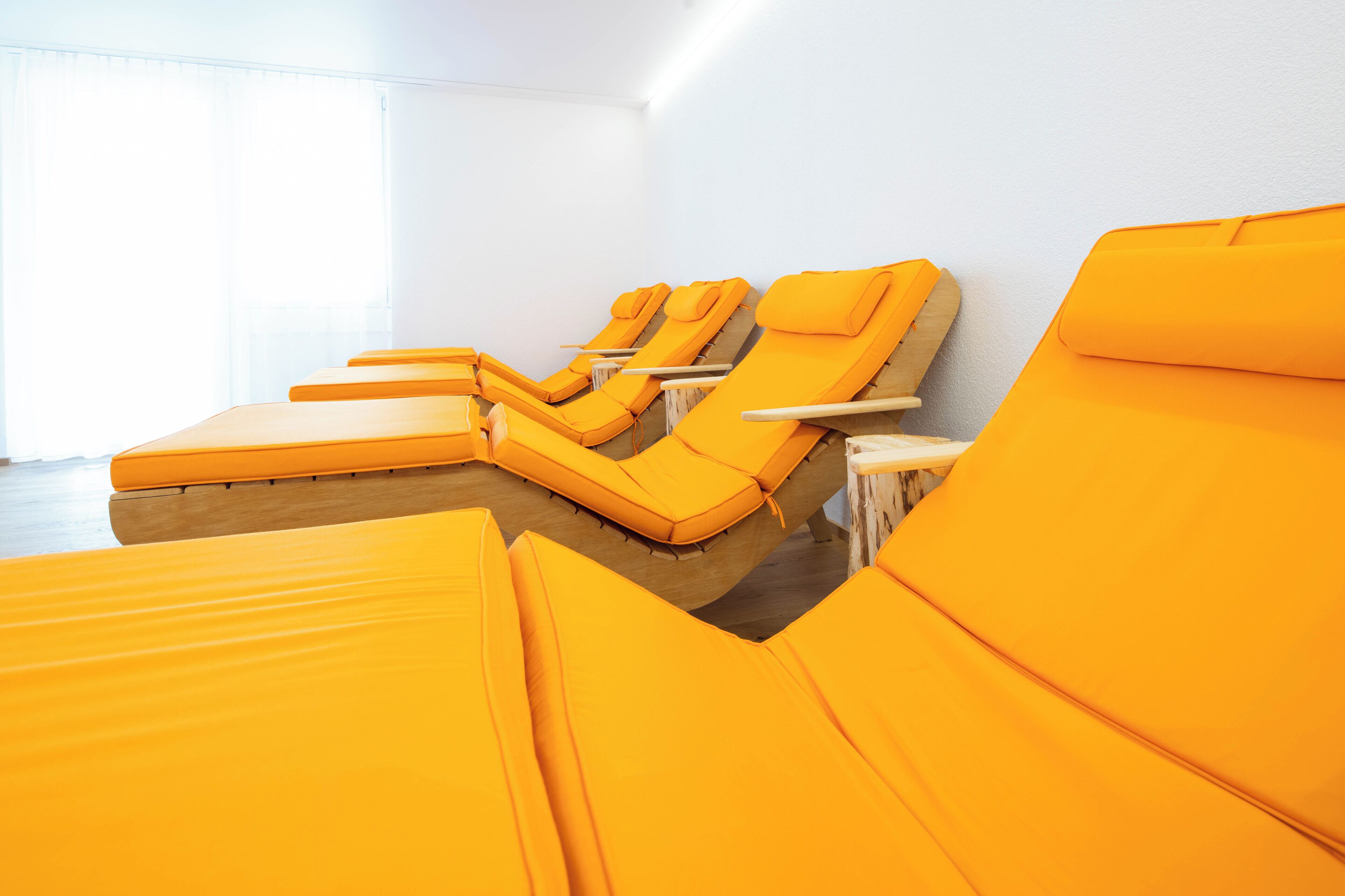 A row of yellow sunbeds in a room with white walls and a large window.