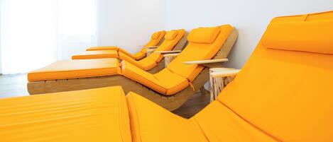 A row of yellow sunbeds in a room with white walls and a large window.