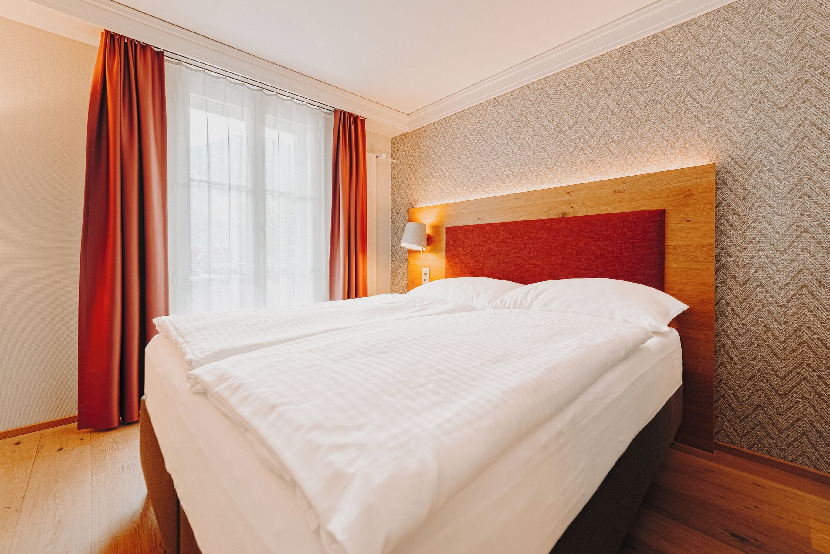 A hotel room with a large bed, wooden headboard, and a patterned wall.