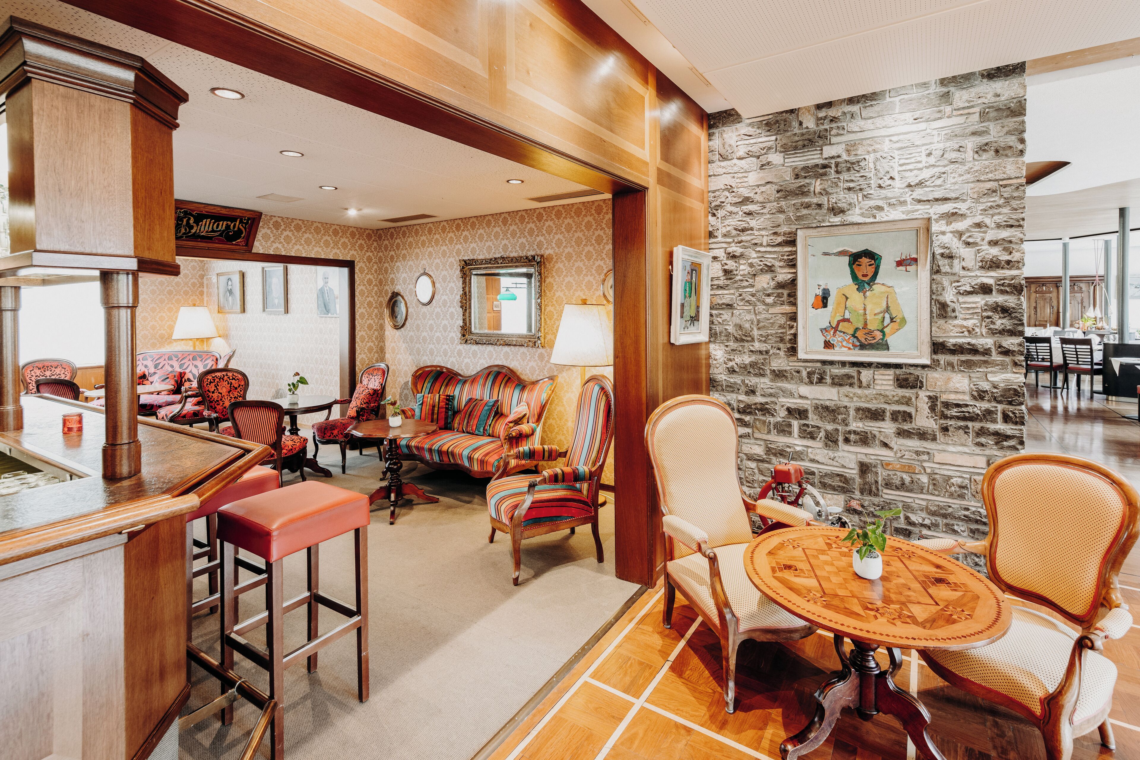 A hotel lobby with a bar area, seating with striped chairs, a stone wall with artwork, and a billiards sign.