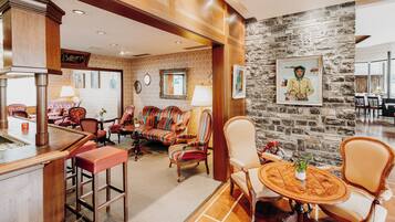 A hotel lobby with a bar area, seating with striped chairs, a stone wall with artwork, and a billiards sign.