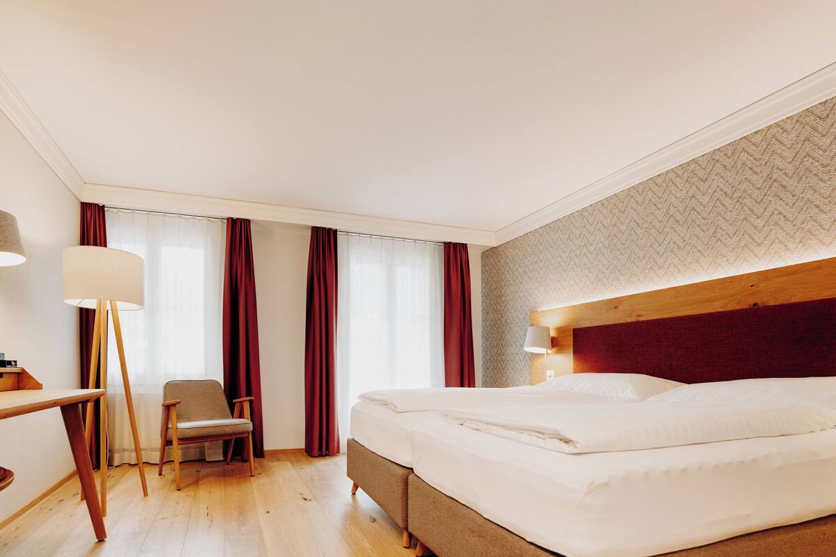 A hotel room with a bed, a desk, a chair, and a lamp.