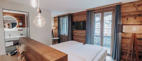 A modern bedroom with a wooden headboard, a large bed, a TV, and a balcony with curtains.