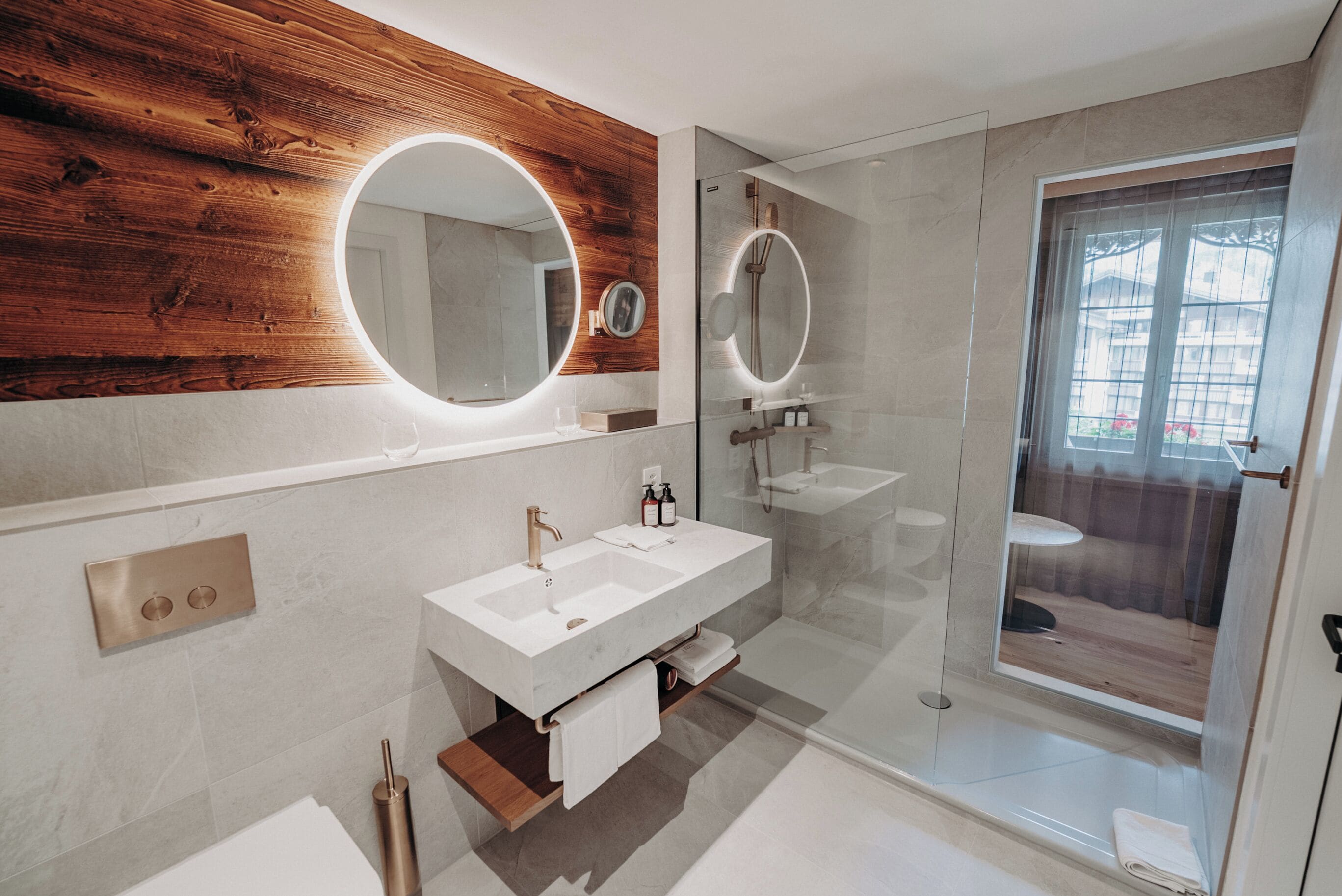 A modern bathroom with two sinks, a wooden accent wall, and a glass shower enclosure.