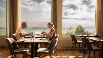 A dining area with a table and chairs, large windows with a view of the sea, and a modern interior design.