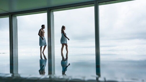A room with large windows, a reflective floor, and a view of the sky.