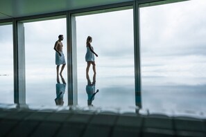 A room with large windows, a reflective floor, and a view of the sky.