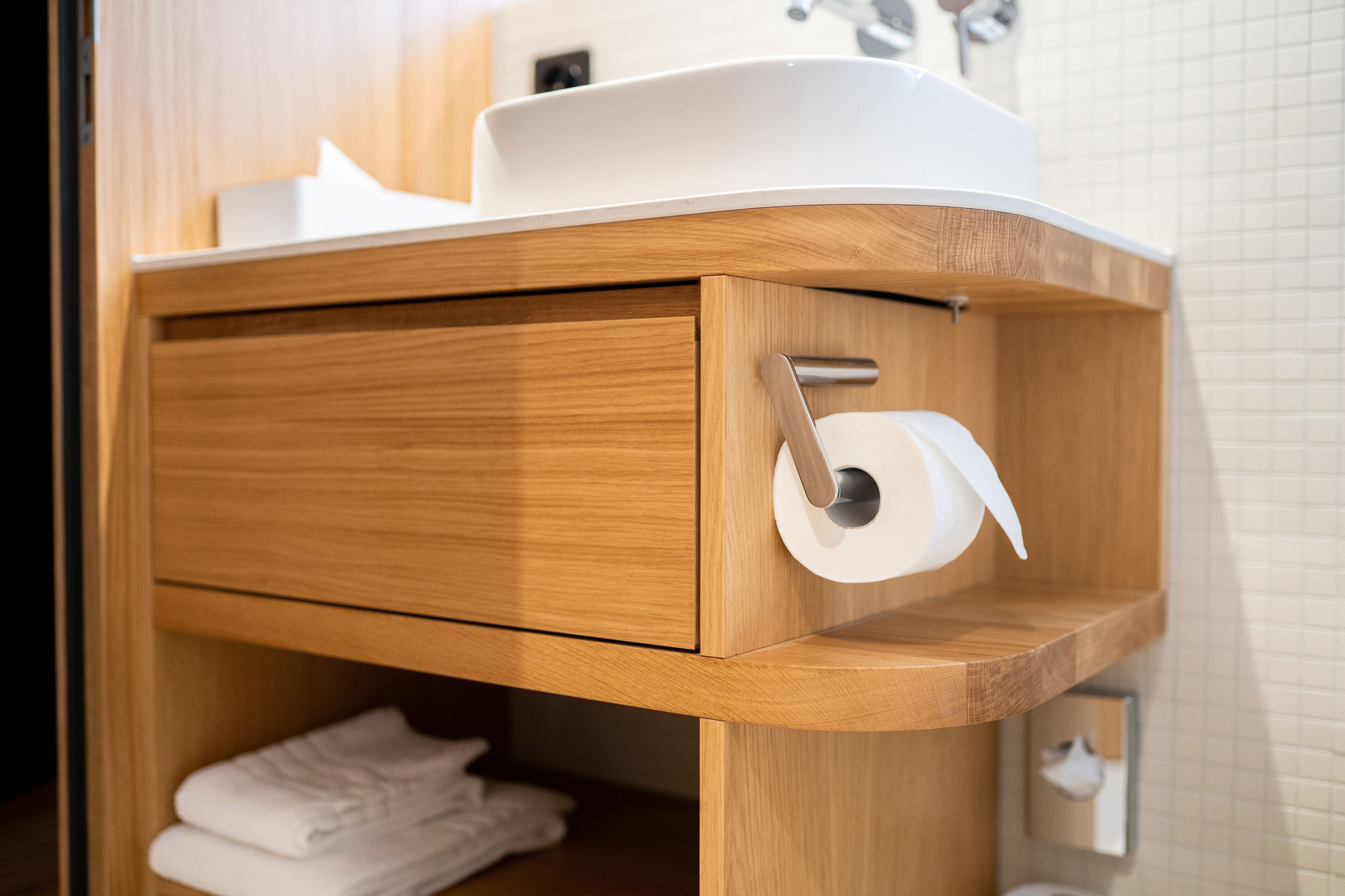 Un tocador de madera con un lavabo blanco, un soporte para toallas y un dispensador de papel higiénico.