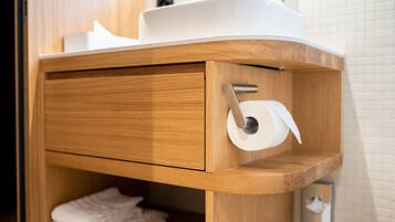 Un tocador de madera con un lavabo blanco, un soporte para toallas y un dispensador de papel higiénico.