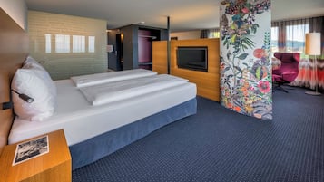 A hotel room with a large bed, a desk with a photo frame, a TV, and a floral-patterned partition.