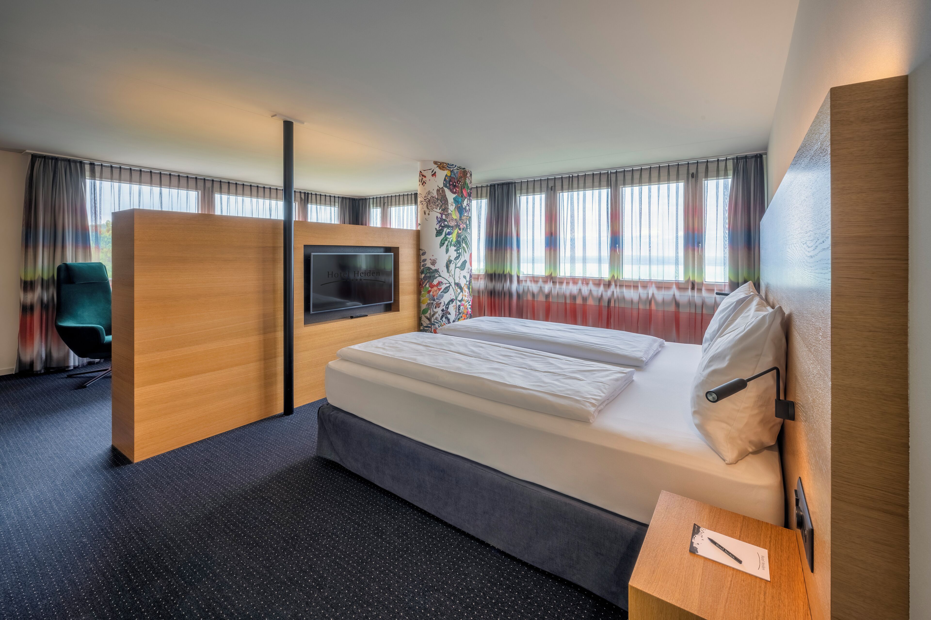A modern hotel room with a large bed, a TV, a desk, and a chair.