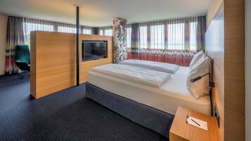 A modern hotel room with a large bed, a TV, a desk, and a chair.