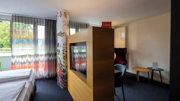 Relax in a stylish room with a comfortable bed, mounted TV, and large window offering a view of the surrounding greenery.