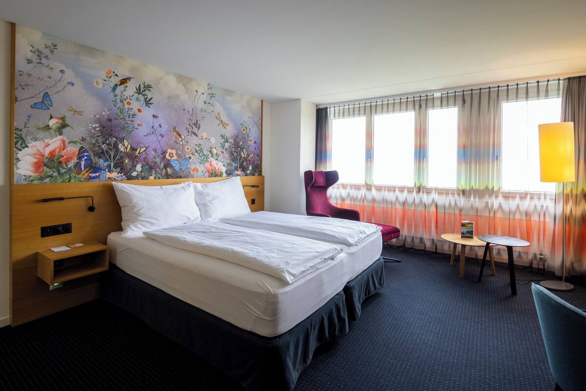 A hotel room with a large bed, a desk, a chair, and a colorful floral mural on the wall.