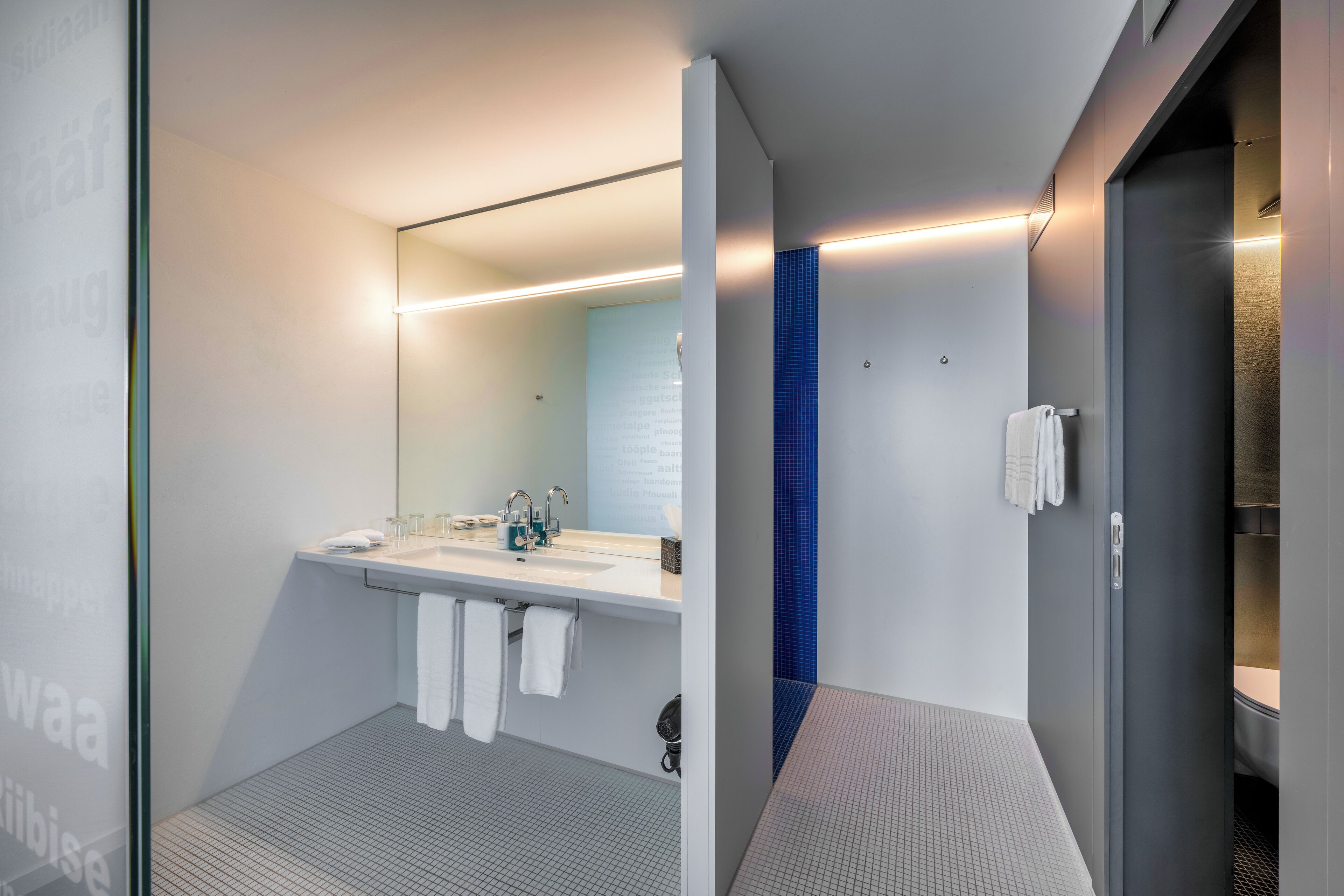 A modern bathroom with a large mirror, two sinks, and a shower area.