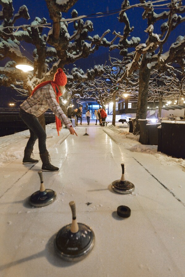 A person playing shuffleboard on an outdoor ice surface at night. - Seehotel Pilatus (Hergiswil)