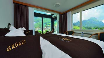 Habitación de hotel con una cama grande, vistas a montañas y una ventana con cortinas.