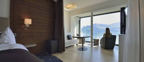 A modern hotel room with a large bed, a sofa, a dining table, and a view of the sea.