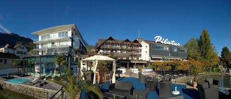 A hotel with a swimming pool, outdoor seating, and a mountain backdrop.